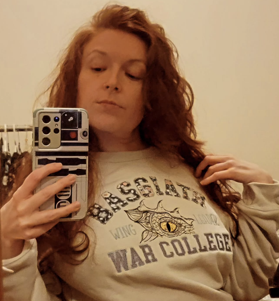 It's me taking a selfie in a mirror, I'm using a phone with an R2-D2 case. I'm wearing a sweatshirt that says "Basgiath War College Wing Leader," which is a reference to The Fourth Wing book series.